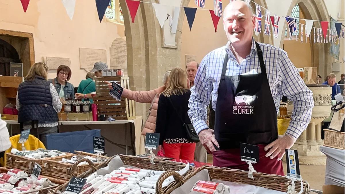 Cotswold Curer at WFOFAD 1600 x 900 px A smiling stallholder in an apron behind his stall inside St Mary’s